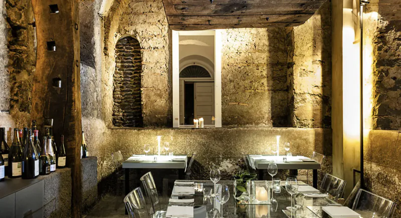 Elegant restaurant with rustic stone walls and arched doorway, set dining tables with wine glasses and candles