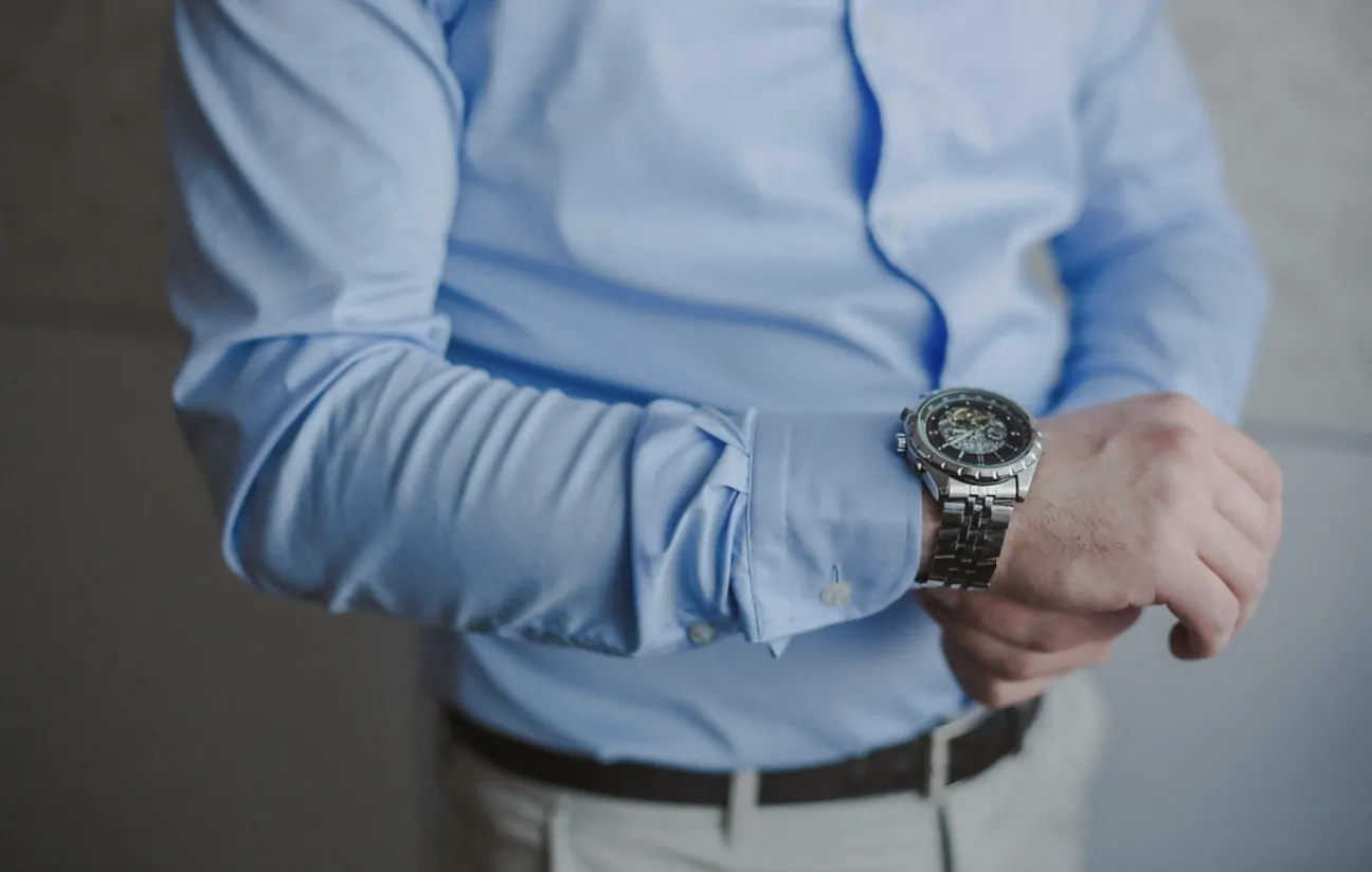 Man in light blue shirt checking silver Omega wristwatch on left wrist