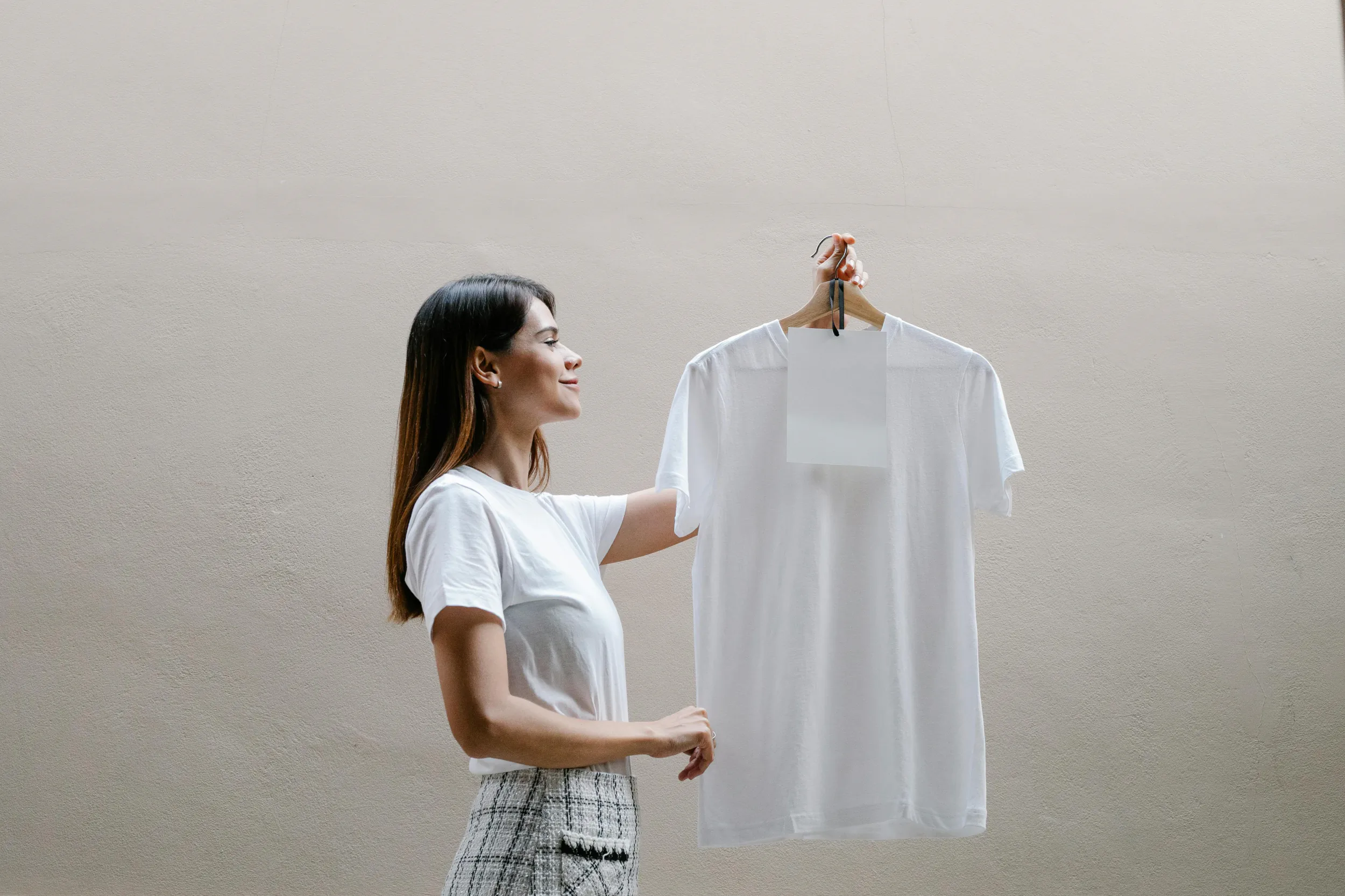 Woman holding up a white t-shirt on a hanger against a plain wall