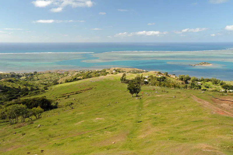 Aerial view of green hills overlooking turquoise lagoon and ocean with scattered trees and houses