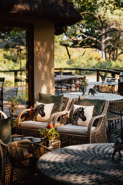 Outdoor patio at Tintswalo Safari Lodge with wicker chairs, zebra-print cushions, and tables overlooking lush greenery