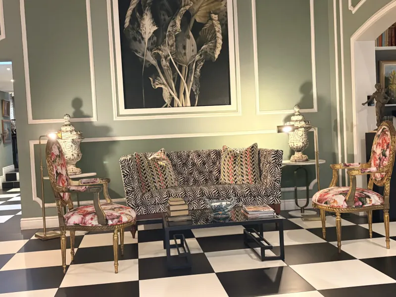 Elegant hotel lounge with black and white checkered floor, patterned sofa, floral armchairs, and large botanical wall art