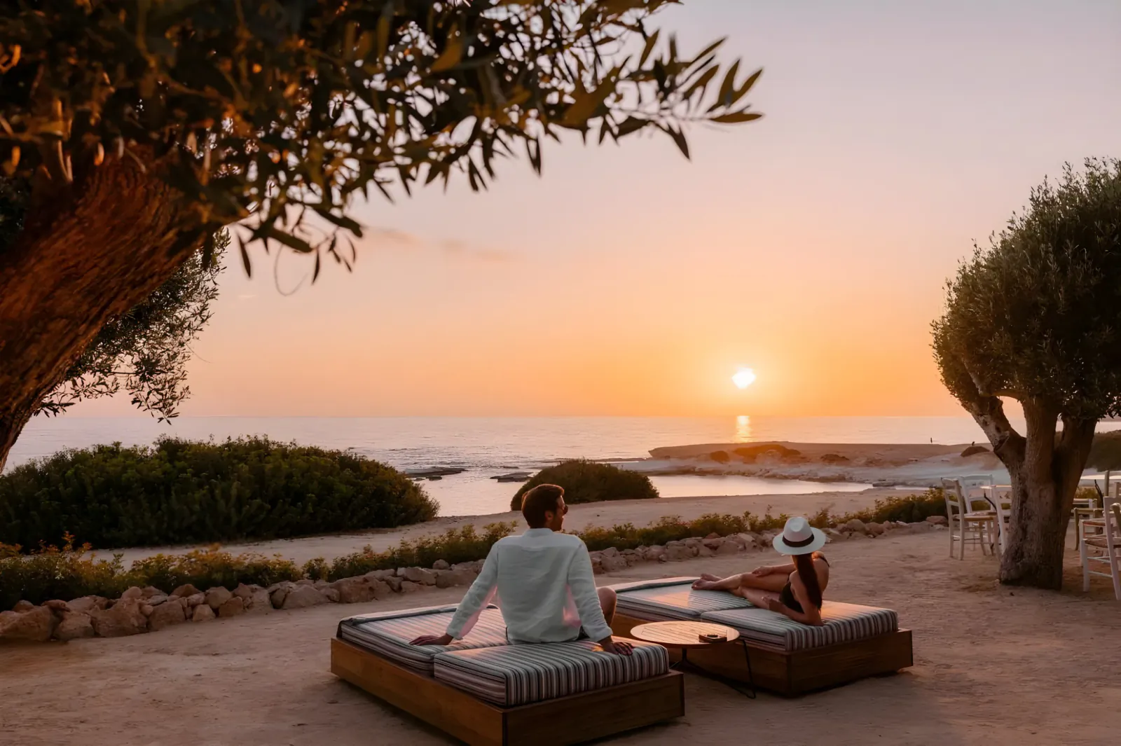Couple relaxing on lounge beds at sunset overlooking the sea at Cap St Georges Hotel & Resort