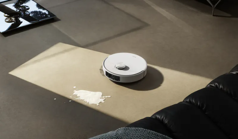 White robot vacuum cleaner on a beige rug with spilled powder on a dark floor