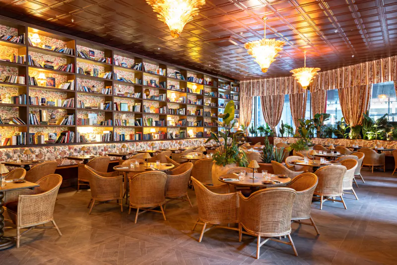 Elegant restaurant interior with floor-to-ceiling bookshelves, wicker chairs, and ornate chandeliers