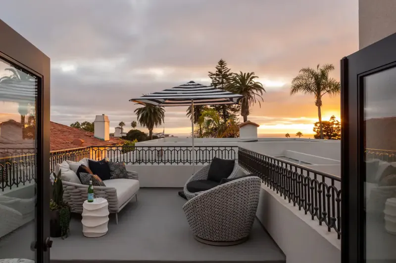 Rooftop terrace at sunset with striped umbrella, woven lounge chairs, and city skyline view