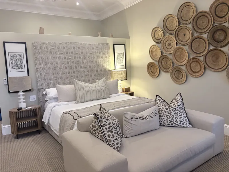 Luxury hotel bedroom with patterned headboard, white bedding, leopard-print pillows, and woven wall decor