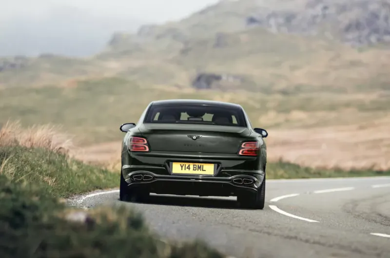 Rear view of a dark green Bentley Flying Spur driving on a winding mountain road