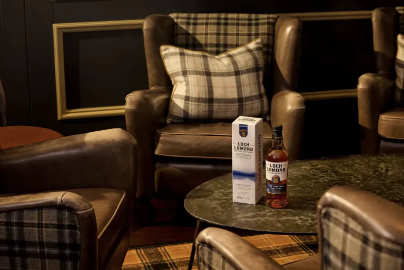 Loch Lomond whisky bottle and box on a marble table in a cozy lounge with leather armchairs and plaid cushions