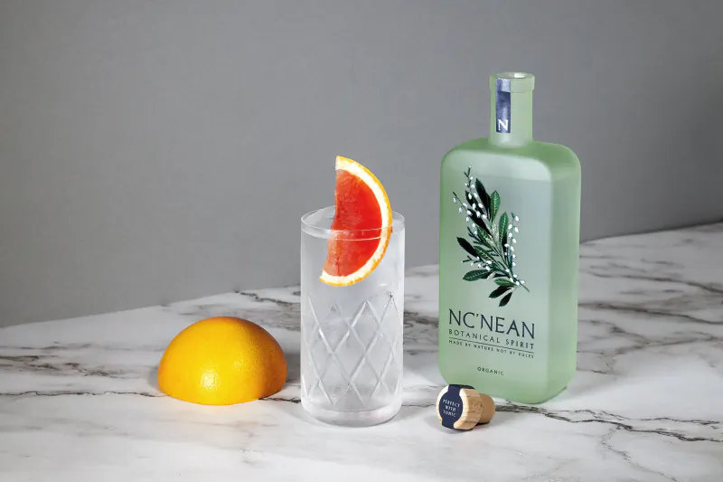 No.1 Nean botanical spirit bottle with glass of drink garnished with grapefruit slice and whole grapefruit on marble surface