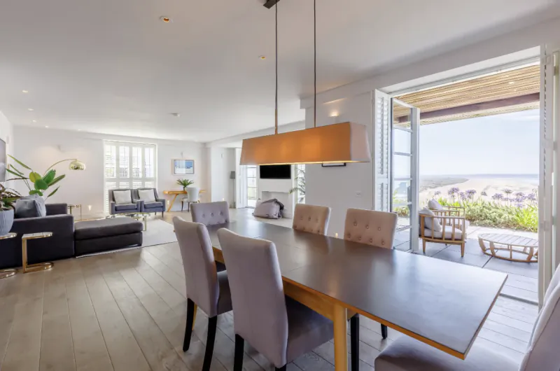 Modern open-plan dining area with long table and grey chairs, leading to a balcony with sea views at The Chalet Apart-Hotel, Saunton Sands