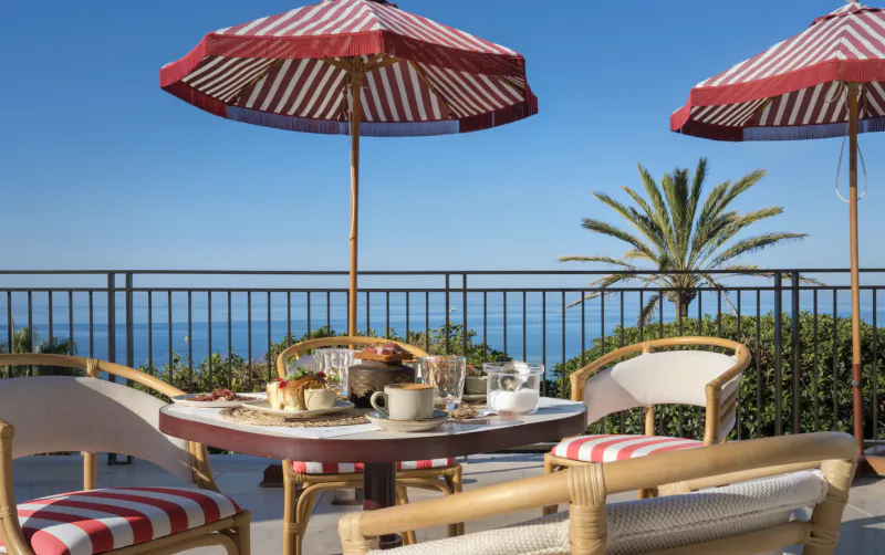 Outdoor terrace table with breakfast under red striped umbrellas overlooking the sea at El Fuerte Marbella