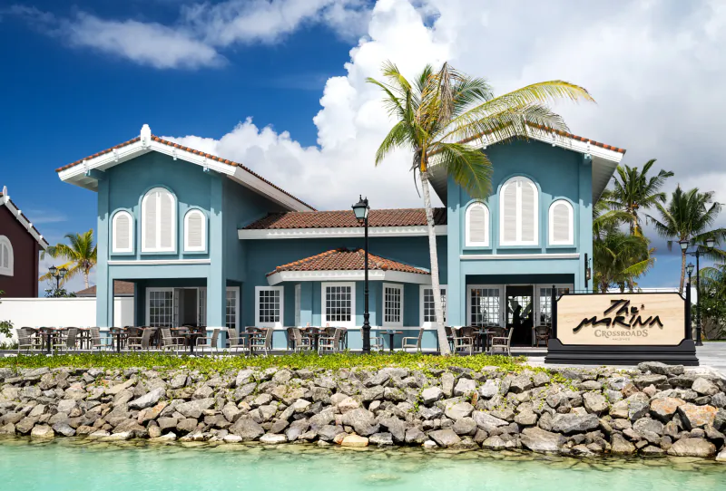 Blue waterfront resort building with palm trees, outdoor seating, and a Marlin sign by the water
