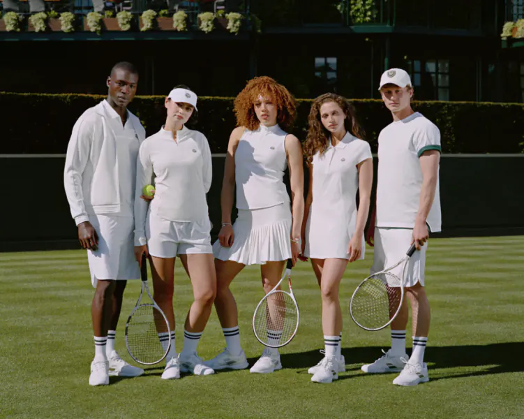 Five diverse tennis players in white outfits pose on a grass court holding rackets at Wimbledon
