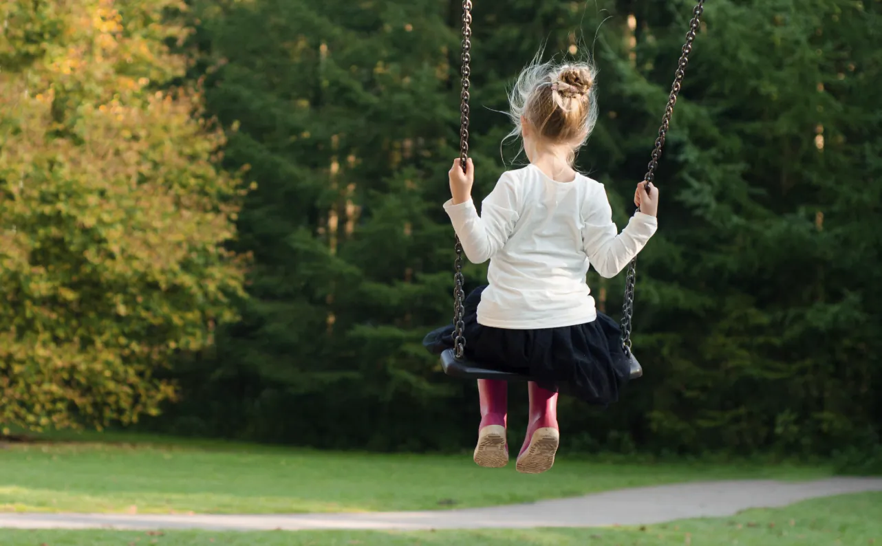 Young girl with hair in a bun swinging on a chain swing in a park, viewed from behind