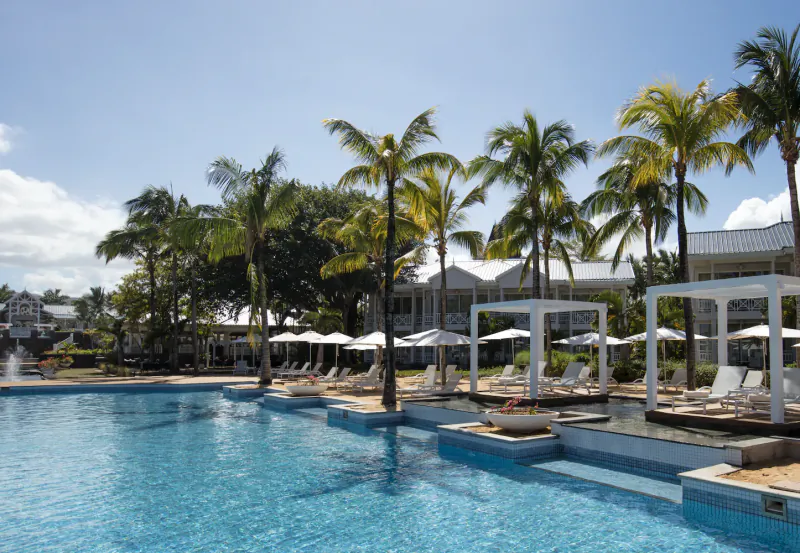 Luxury resort pool with palm trees, white cabanas, and lounge chairs under a clear blue sky