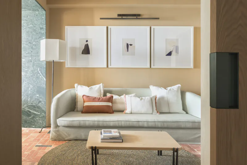 Modern living room with light sofa, white and terracotta pillows, wooden coffee table, three abstract artworks, and floor lamp