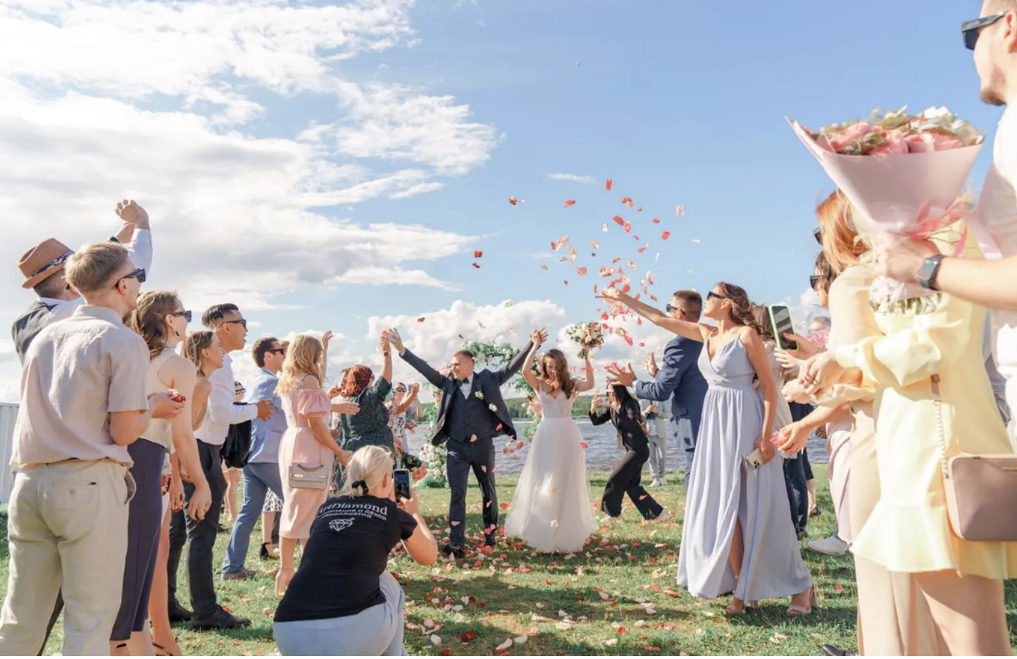 Wedding party tossing rose petals outdoors as bride and groom celebrate on a sunny day