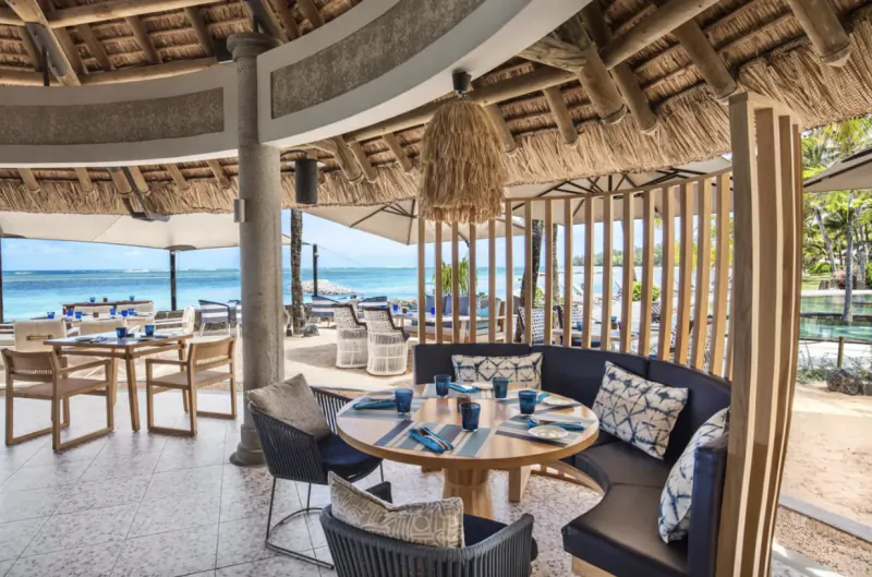 Oceanfront restaurant with thatched roof, round table set with blue glassware, and panoramic sea view