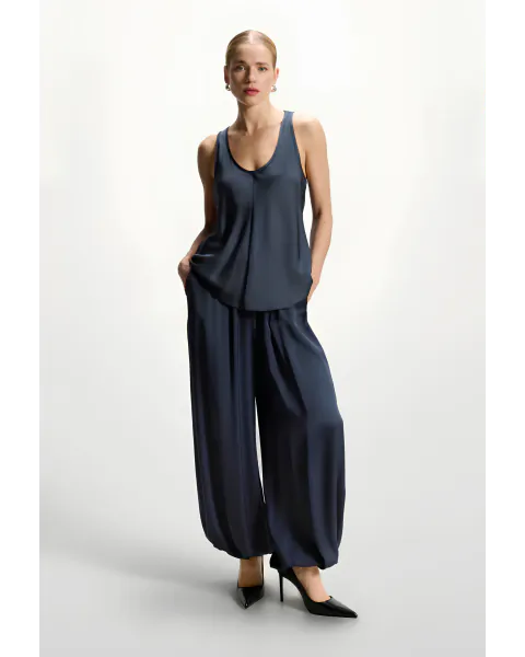 Woman in navy satin tank top and wide-leg trousers with black heels, hands in pockets, studio pose
