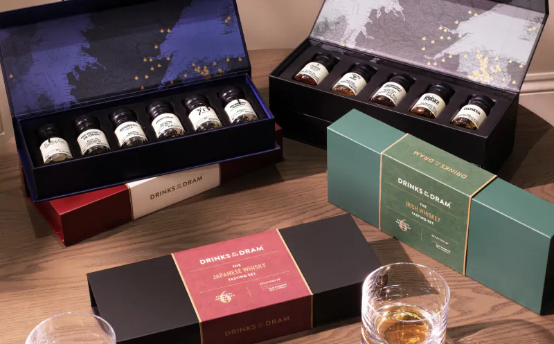 Drinks by the Dram whisky tasting sets in open gift boxes with sample bottles and two glasses on a wooden table