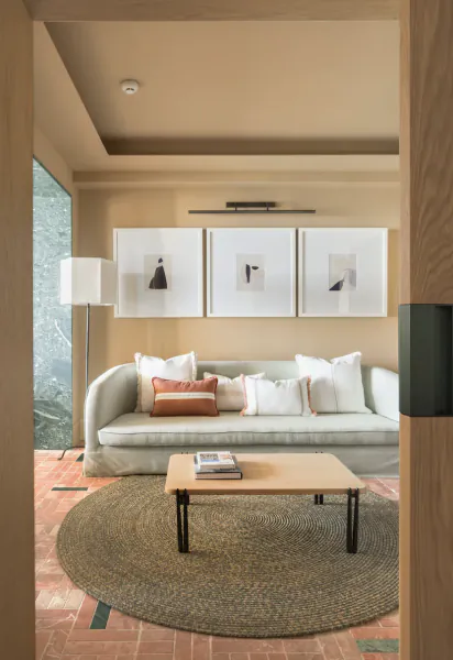 Modern living room with light gray sofa, wooden coffee table on round woven rug, three framed artworks, and floor lamp