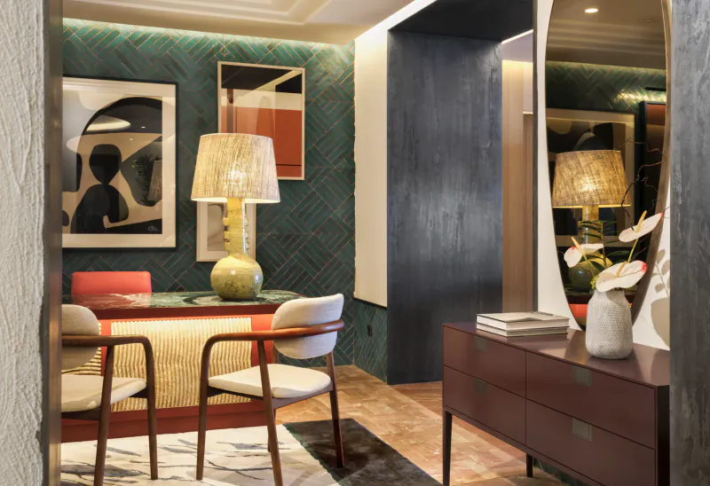 Modern dining area with red table, white chairs, green herringbone wall, abstract art, and tall mirror with lamps and vase on console