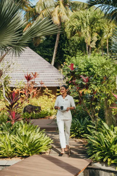 Woman in white uniform walking on wooden path with coffee cup in tropical resort garden