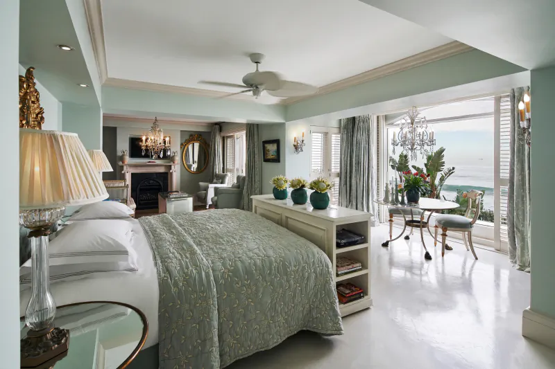 Luxury hotel bedroom with sea view, large bed, seating area, and dining table by open balcony doors