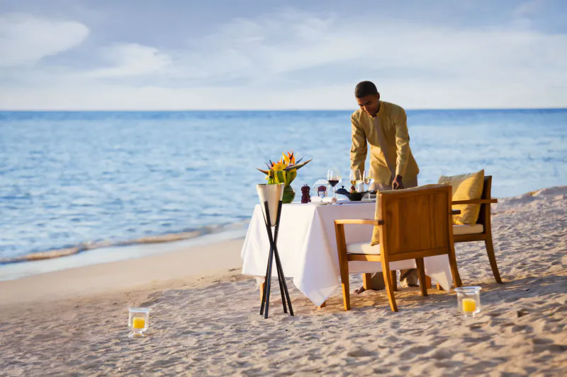 Waiter setting a romantic beachfront dining table with white tablecloth and flowers at Le Jadis Beach Resort, Mauritius