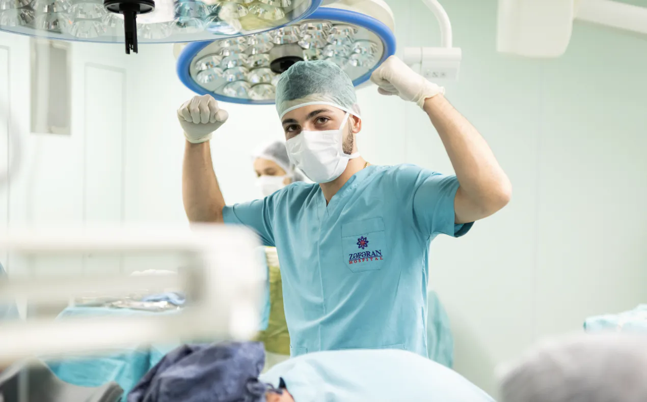 Surgeon in blue scrubs raising arms in celebration under operating room lights