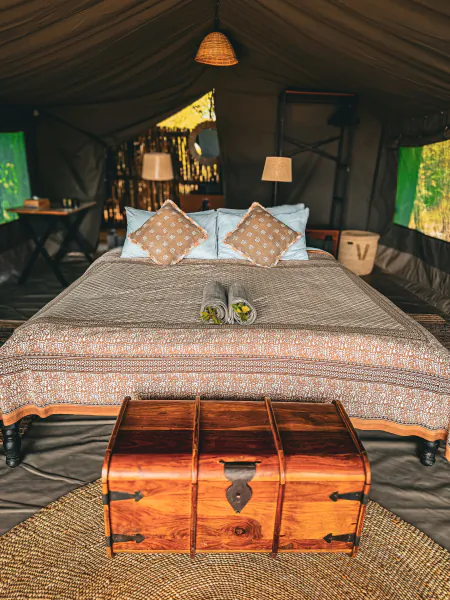 Luxury safari tent bedroom with large patterned bed, wooden chest at foot, and open views to the savanna