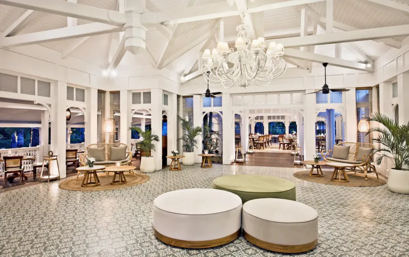 Spacious white luxury lounge with patterned tile floor, large ottomans, sofas, chandelier and arched windows at dusk