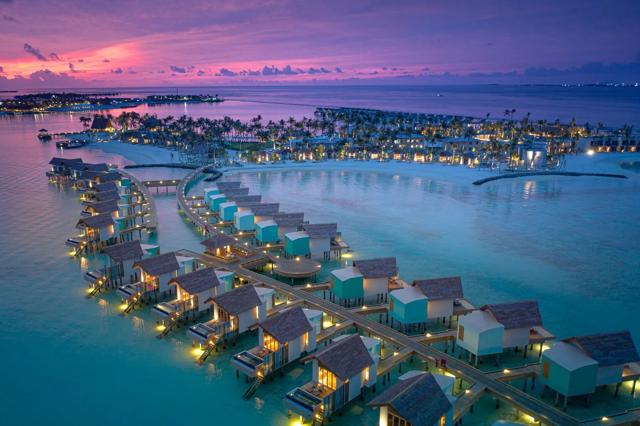 Aerial view of overwater villas with glowing lights at dusk in the Maldives