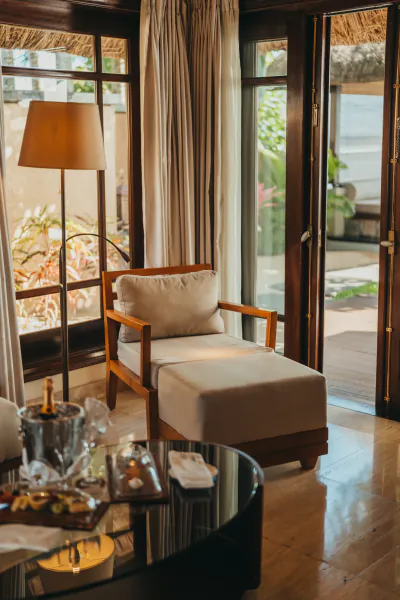 Luxury lounge chair with ottoman beside open doors to a tropical patio, ice bucket and snacks on a glass table in the foreground