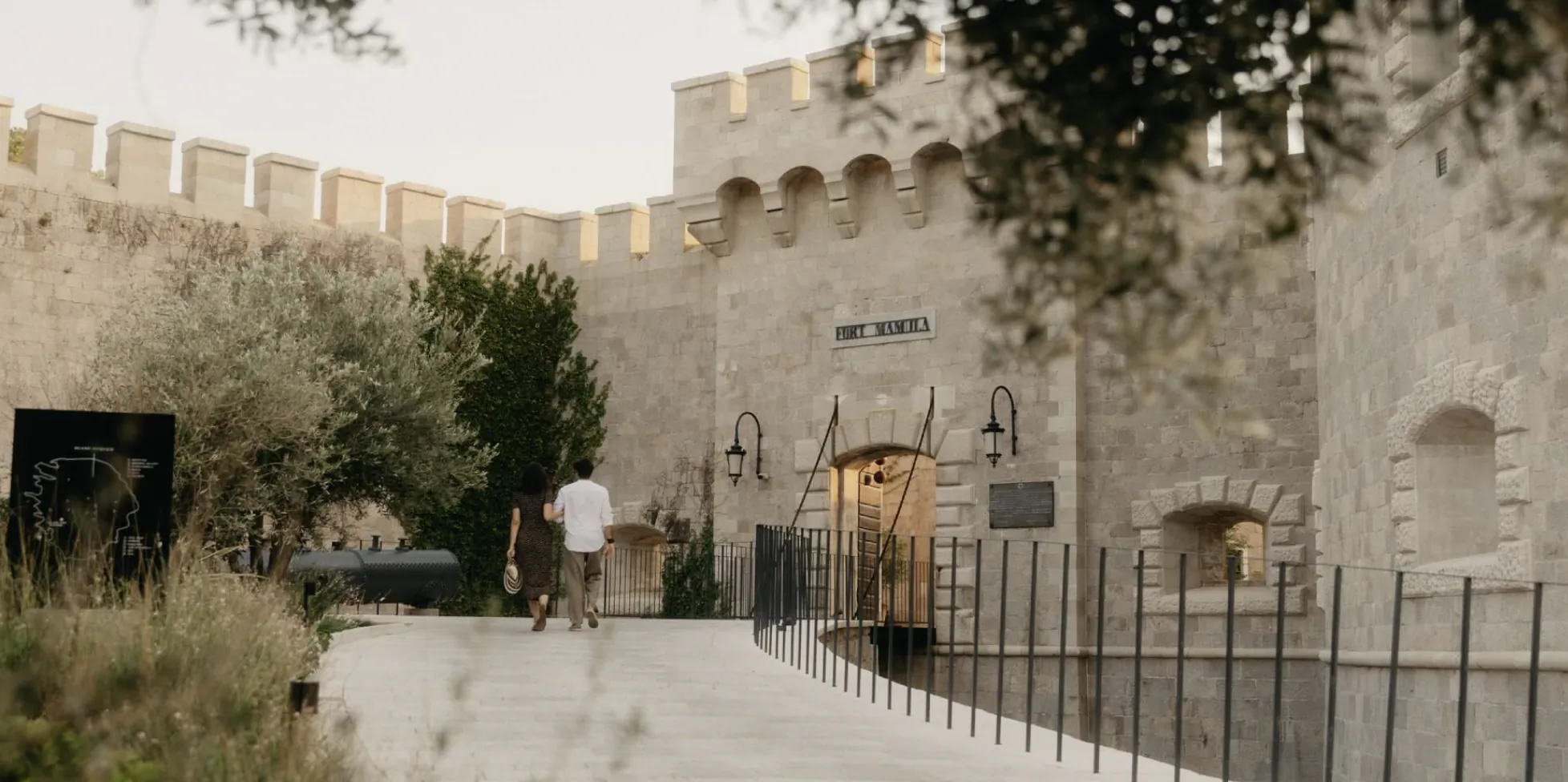 People walking toward the entrance of Fort Mamula, a historic stone fortress with battlements