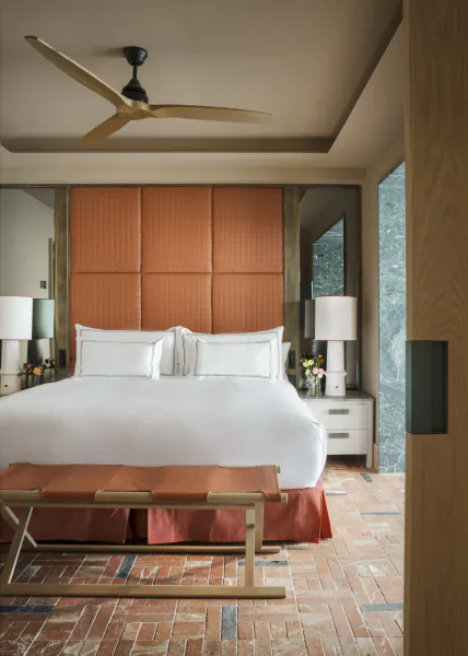 Modern bedroom with large white bed, terracotta upholstered headboard, ceiling fan, and terracotta tile floor