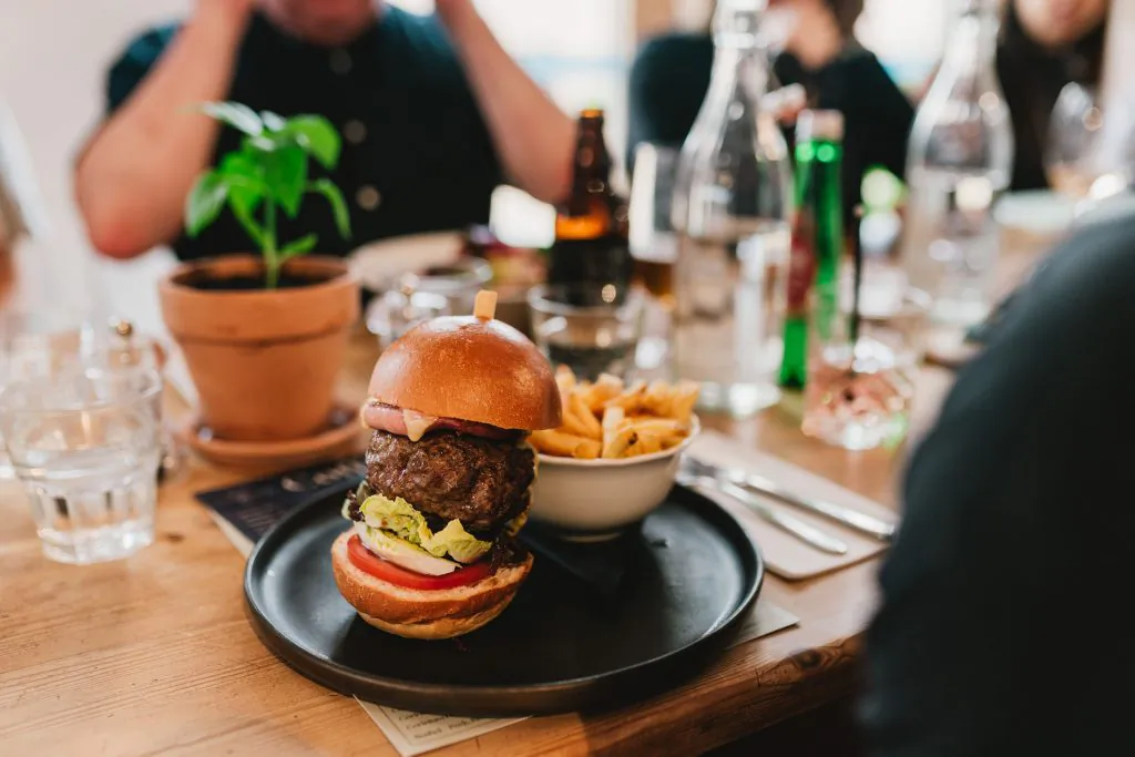 Gourmet burger with beef patty, tomato, avocado and bun on black plate with fries at Roots + Seeds Café & Kitchen