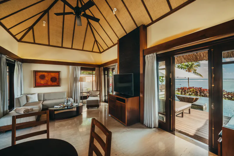 Spacious luxury villa living room with high thatched ceiling, sofa, TV, and open doors to ocean view deck
