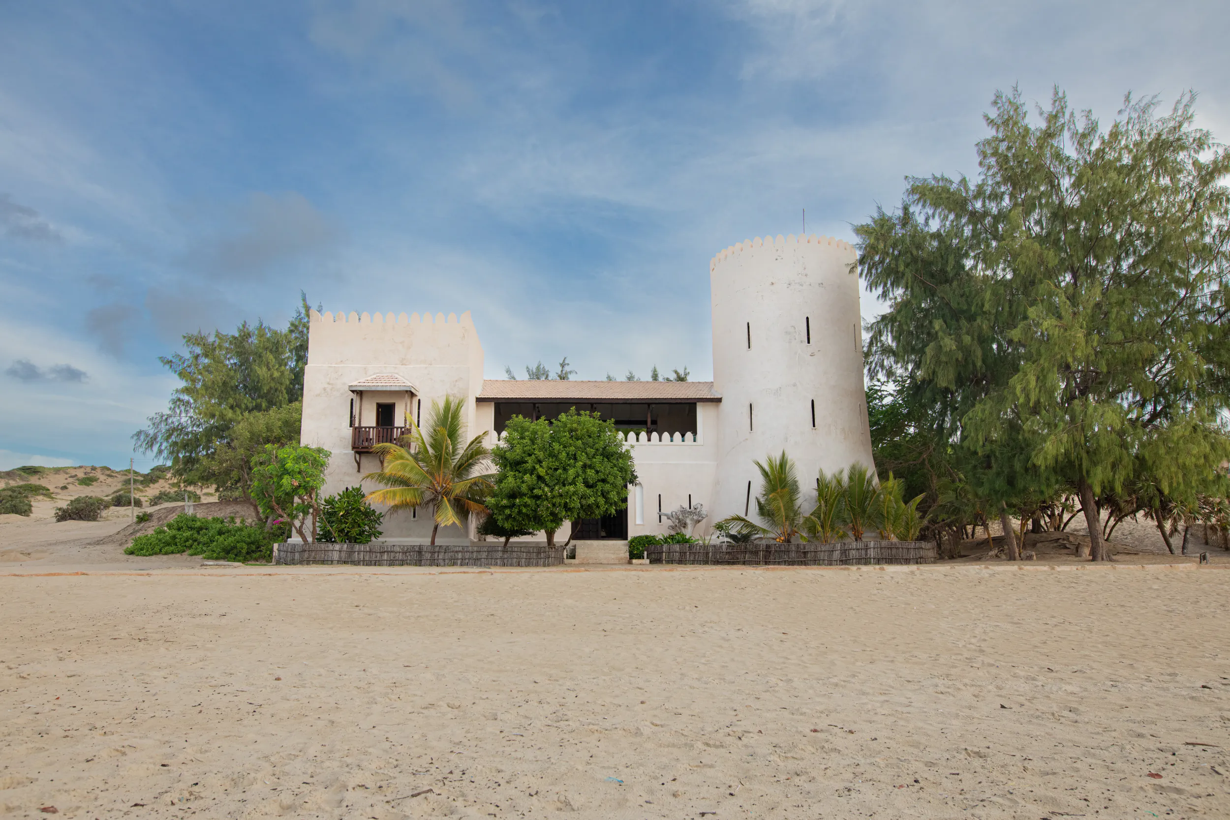 Fort Shela Kenya: white fort-style villa with towers on sandy dunes surrounded by palm trees and greenery