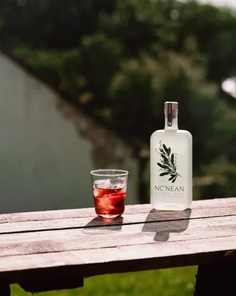 NCNEAN botanical spirit bottle and glass of red drink on wooden table outdoors
