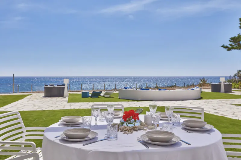 Elegant outdoor dining table with white linens and red flowers overlooking the sea at a luxury villa