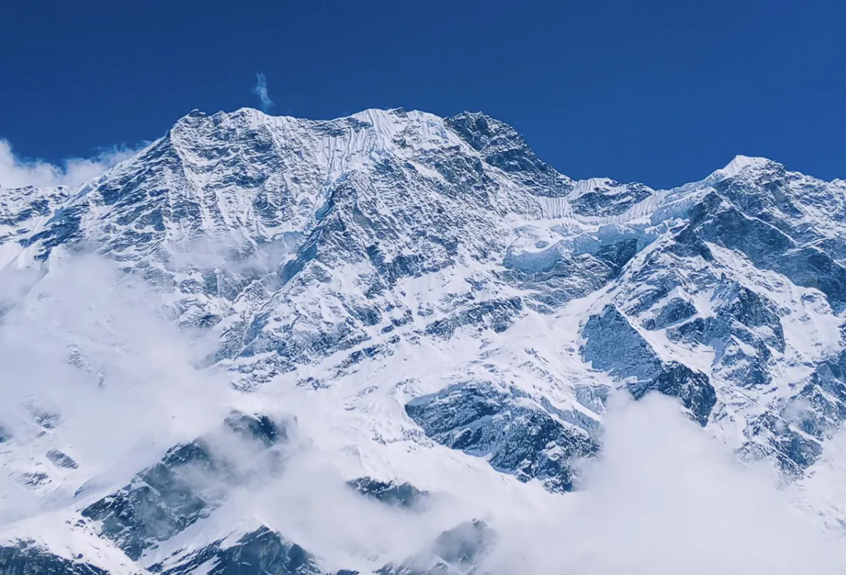 Snow-covered Himalayan peaks under clear blue sky with clouds below