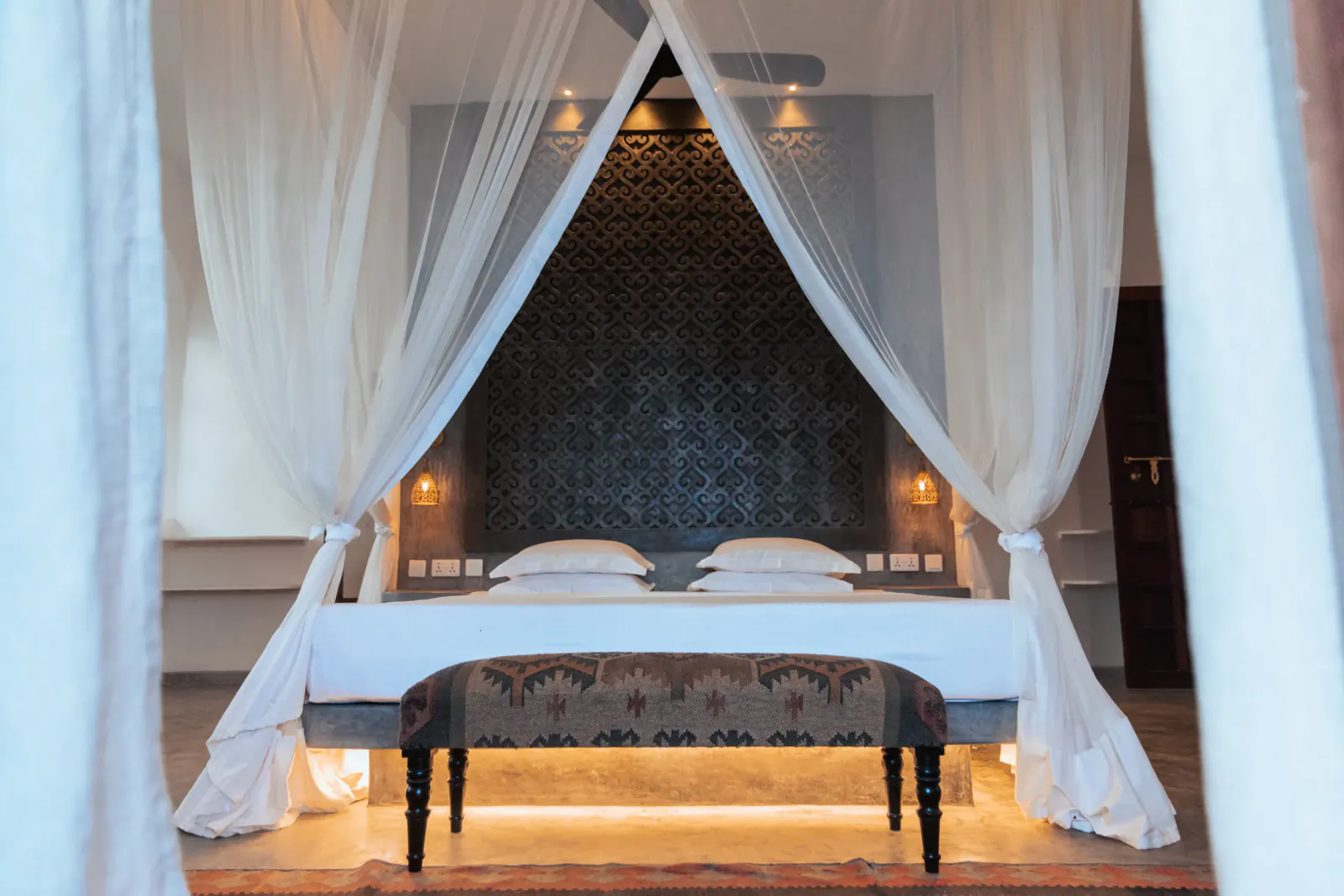 Four-poster canopy bed with white linens and sheer curtains in a luxury bedroom at The Fort Shela Kenya villa