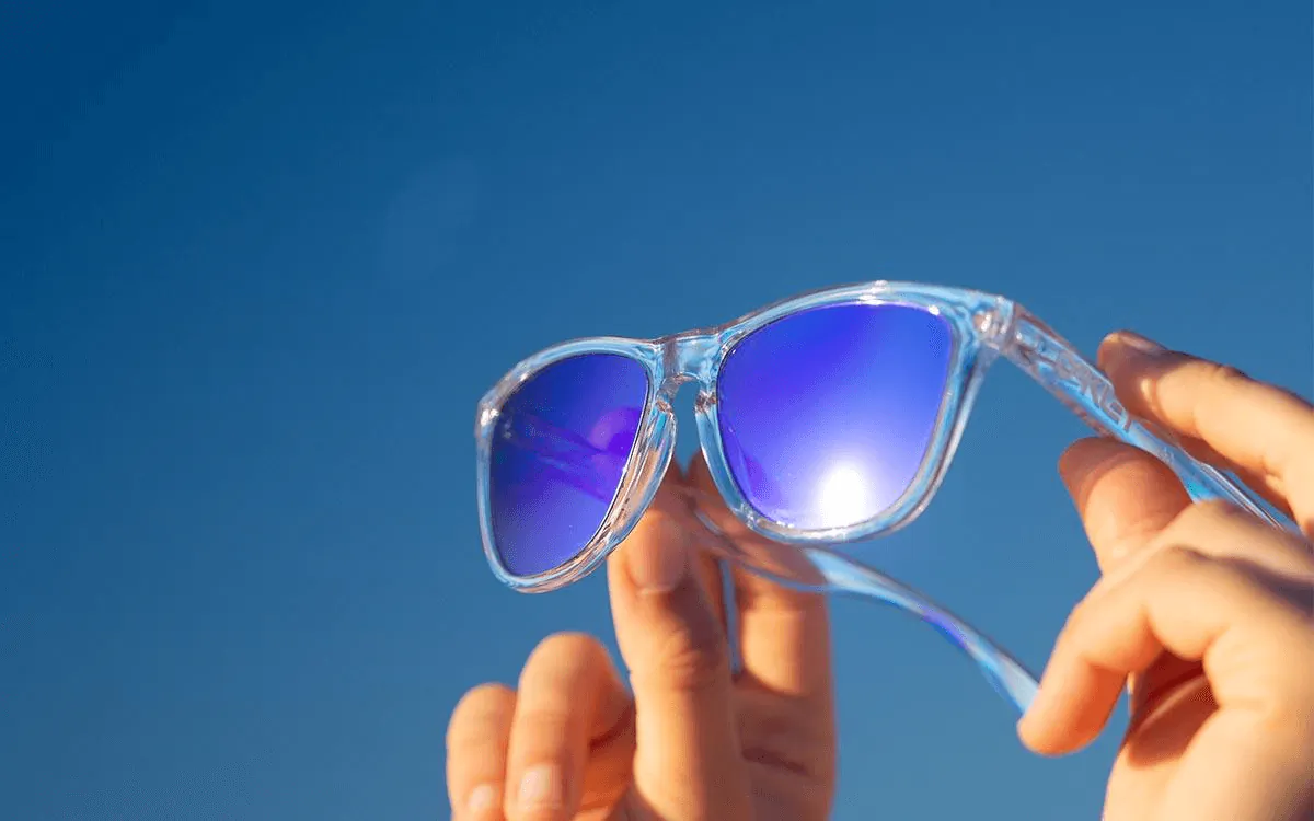 Hands holding blue reflective sunglasses against a clear sky