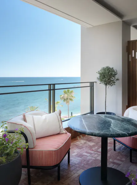 Balcony with pink armchair overlooking the sea, marble table, and potted plants on a sunny day