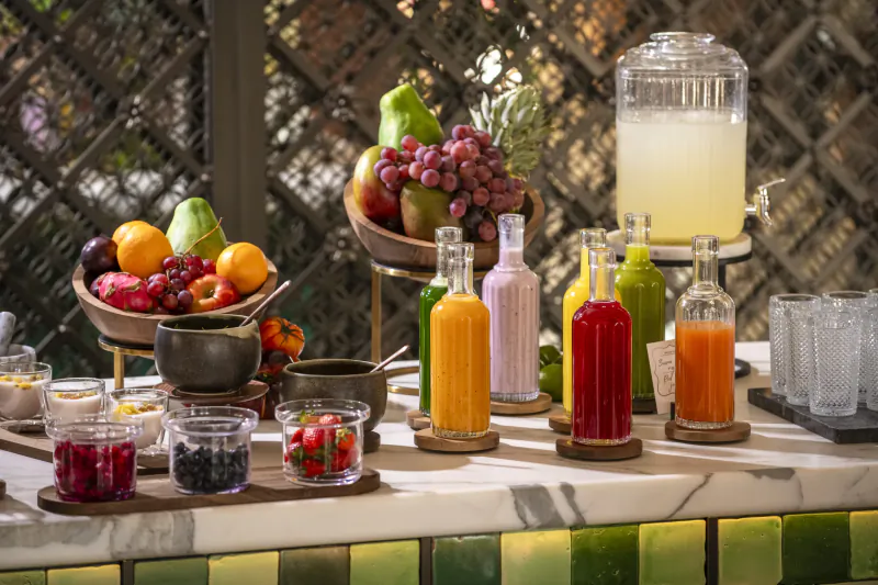Colorful fruit display and assorted juice bottles on a marble bar counter with a large dispenser
