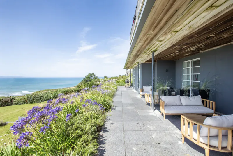 Modern seaside hotel patio with outdoor sofas overlooking ocean and purple flowers at Saunton Sands
