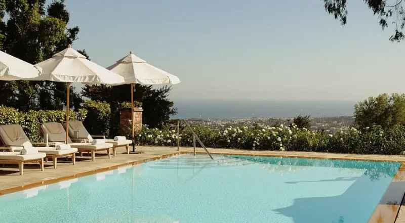 Luxury infinity pool overlooking the ocean with lounge chairs and white umbrellas on a sunny terrace