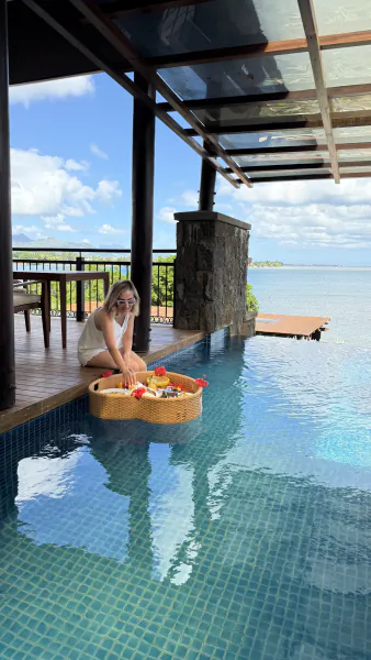 Woman in white dress sitting poolside with floating breakfast basket at Le Jadis Beach Resort Mauritius